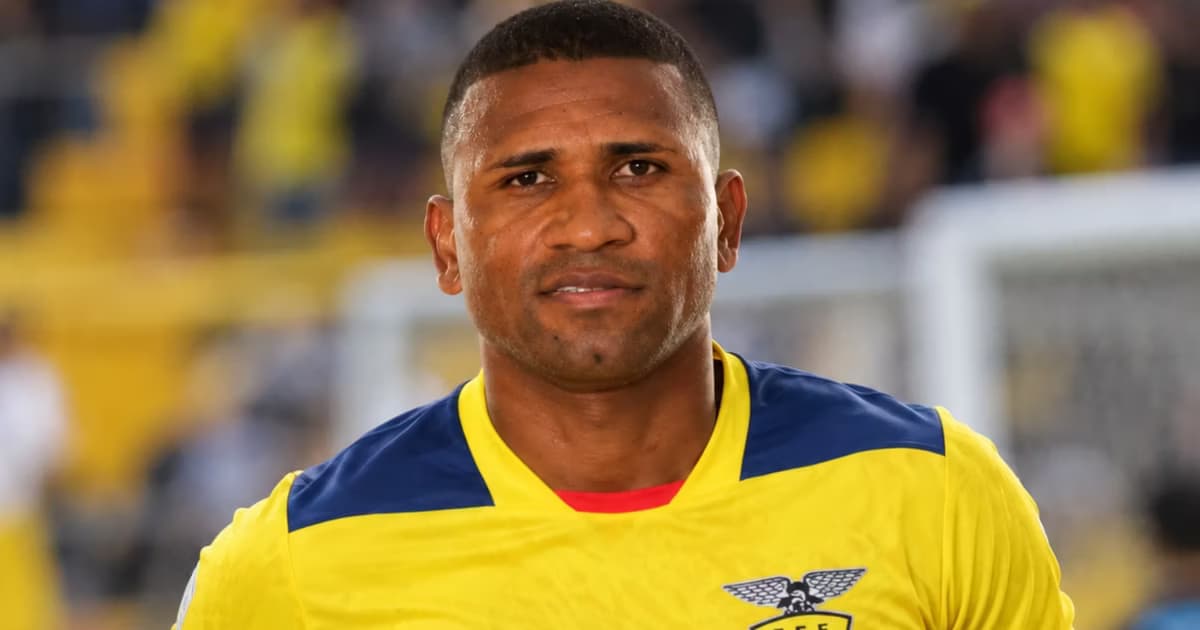 Jorge Guagua con camiseta amarilla de Ecuador y un estadio de fútbol desenfocado al fondo.